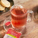 A glass mug of Bigelow Cinnamon Apple Herbal Tea with a tea bag in it on a plate with cookies.