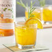 A glass of Monin candied orange juice with ice and a slice of orange.