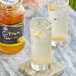 A glass of Assi ginger tea with ice and fruit next to a jar of tea.