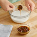 A person pouring Fabbri Malaga Marsala / Rum Raisin flavoring paste into a bowl of brown liquid.