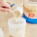 A hand pouring Premier Protein vanilla powder into a container.