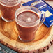Two glass mugs of Ghirardelli hot chocolate on a wood surface.