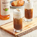 Two glasses of brown drinks with white cream on top using Monin Hazelnut Syrup.