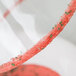 A close up of a glass with a watermelon cocktail rimmed with red and green sugar.