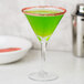 A close up of a green drink in a martini glass with a red rim and lime garnish.