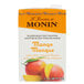 A case of Monin Mango Fruit Smoothie Mix on a table in a smoothie shop.