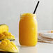 A glass of Monin Mango smoothie with a straw in it.