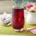 A glass of Bossen Rose Garden fruit tea on ice with a straw on a table with a white vase of flowers.