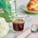 A glass cup of Lavazza Tierra! Brasile Intense coffee on a table with a spoon and bag of coffee.