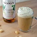 A glass cup of coffee with whipped cream and Monin Macadamia Nut Syrup.