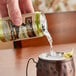 A hand pouring Goslings Citrus Tonic Water into a copper cup on a table with ice.