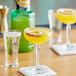 A table with a bottle of Finest Call Pornstar Martini Mix and a glass of yellow liquid with a slice of fruit in it.