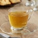 A glass cup of Bigelow Cozy Chamomile tea on a saucer with a cookie.