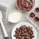 A table with Callebaut dark chocolate chips and a bowl of chocolate sauce.