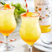 Two glasses of Monin passion fruit syrup mixed with orange juice on a table.