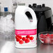 A white jug of Torani Raspberry Fruit Smoothie Mix with a pink label next to a bowl of raspberries.