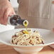 A person pouring white truffle oil onto a bowl of spaghetti with mushrooms.
