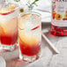 Two glasses of fruit juice with Monin Stone Fruit Syrup on a table in a cocktail bar.