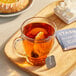 A wooden tray with a glass mug of Stash Decaf Earl Grey tea and a Stash Decaf Earl Grey tea bag next to a pastry.