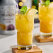 A glass of yellow Monin Passion Fruit Puree garnished with lemon and mint leaves on a table.