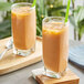 Two glasses of orange Thai tea with straws on a table.