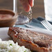 A person sprinkling Regal pink Himalayan salt on a piece of meat with rice and peas.