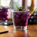 A glass of Monin wild grape syrup with a purple drink and ice.