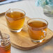 A wooden tray with two glass cups of Numi Organic Jasmine Pearls green tea and a jar of honey.