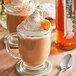 A glass mug of coffee flavored with SHOTT Spiced Pumpkin syrup with a spoon on the table.