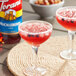Two glasses of red huckleberry drinks on a table with a bottle of Torani Huckleberry syrup.