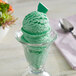 A glass cup of green ice cream with a spoon in it.