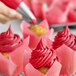 A close-up of a cupcake with pink frosting decorated with a tulip design in red and white.