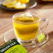 A glass cup of Bigelow Green Tea with a tea bag on a wooden table.