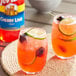 Two glasses of cherry limeade on a table with a bottle of Torani Cherry Lime Flavoring.