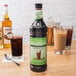 A close-up of a Monin bottle of cold brew coffee concentrate on a table next to a glass of liquid.