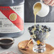 A person pouring Nielsen-Massey vanilla paste into a bowl of blueberries.