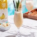 A glass of Island Oasis banana smoothie on a table with a straw.