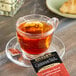 A glass cup of Bigelow cinnamon stick tea on a saucer with a tea bag.