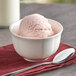 A bowl of pink ice cream with a spoon on a white background.