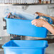 A person holding a blue Vollrath polypropylene food storage container with a standard lid.