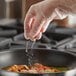 A person in gloves sprinkling Regal Organic Onion Powder onto food in a pan.