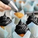 A hand using a pastry brush to frost a cupcake with black frosting.