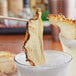 A pair of chopsticks holding a dried pineapple half slice in a glass of liquid.