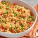 A bowl of rice with peas, tomatoes, and annatto on a cloth with a spoon.