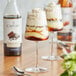 A bottle of Capora chocolate flavoring syrup on a table with a glass of brown and white liquid.