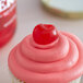 A cupcake with pink frosting and a Regal Maraschino cherry on top.