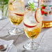 A glass of peach iced tea with fruit and ice on a table.