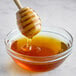 A honey dipper dripping into a bowl of honey.
