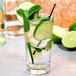 A glass of water with lime slices and mint leaves with a black straw.