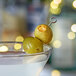 A martini glass with green olives on a stick.